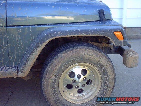 Mud-splattered blue Jeep Wrangler front fender and wheel, showing a Trail Aid tire and aftermarket rim