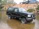 1988 Ford Bronco - This black Ford Bronco is navigating a shallow body of water with a rocky bank in the background.