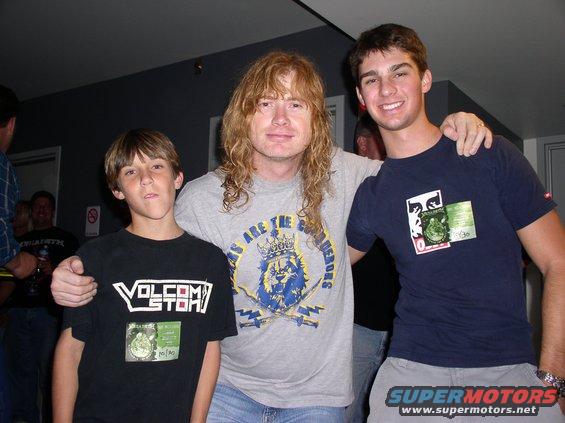 Three people, including Dave Mustaine, pose for a photo. The person on the left wears a Volcom t-shirt
