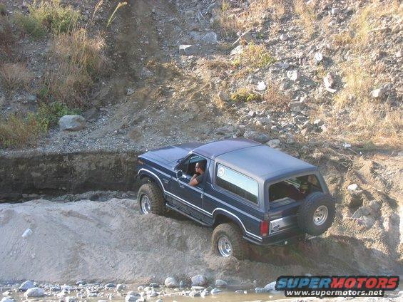 Blue Ford Bronco driving through a sandy, rocky ditch