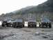 1992 Ford Bronco - Four Ford Broncos are lined up on a rocky beach, with a mountain range visible behind them.
