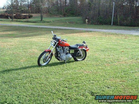 Orange Harley-Davidson motorcycle parked on grass. Text on side reads SUPERMOTORS