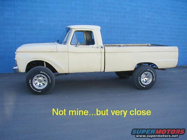 Cream-colored 1965 Ford F-100 pickup truck, lifted with off-road tires, viewed from the side against a blue wall