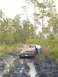 1989 Ford Bronco - A pickup truck is stuck in the mud on a trail, with a person attending to the rear of the vehicle.