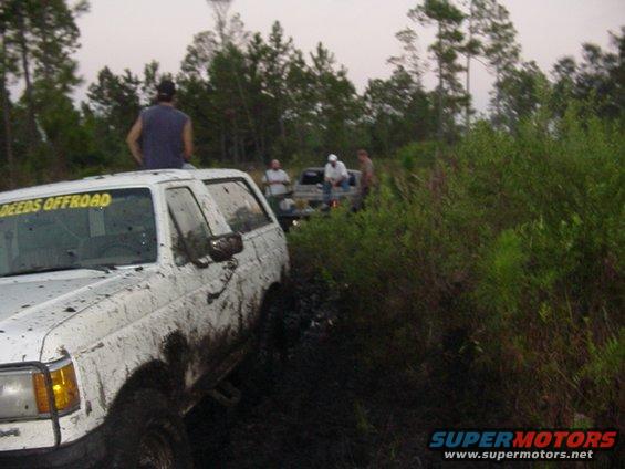 Muddy 1989 Ford Bronco stuck in mud with other vehicles behind it