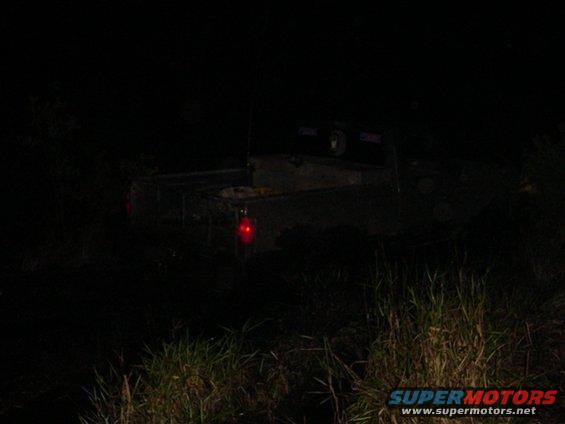 Pickup truck with red taillight visible, parked in grassy area at night