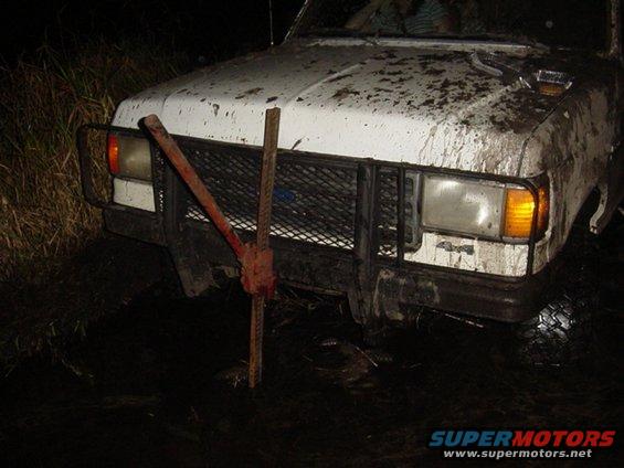White Ford Bronco stuck in mud with a Hi-Lift jack attached to the front bumper