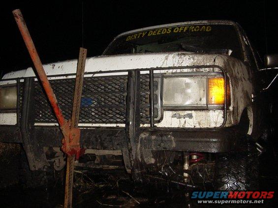 White Ford Bronco stuck in mud, front view, with a jack on the grille