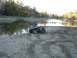 1995 Mercury Grand Marquis - An all-terrain vehicle sits on a muddy shore beside a calm lake with trees in the background.