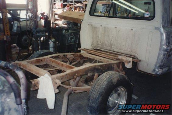White 1967 Ford F-100 truck chassis with rusted frame, viewed from the side in a workshop