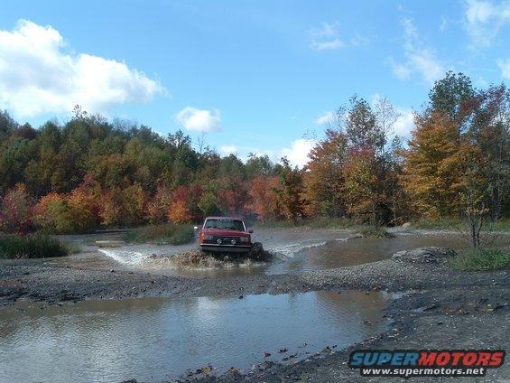 Red SUV driving through a muddy puddle with autumn trees in the background