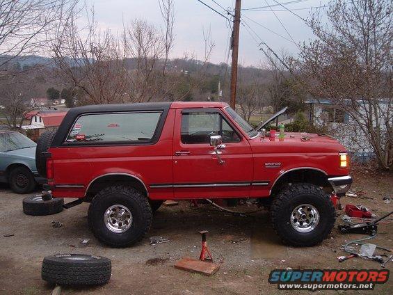 red 1987 Ford Bronco with lifted suspension and off-road tires, hood up, parked outside with tools around it