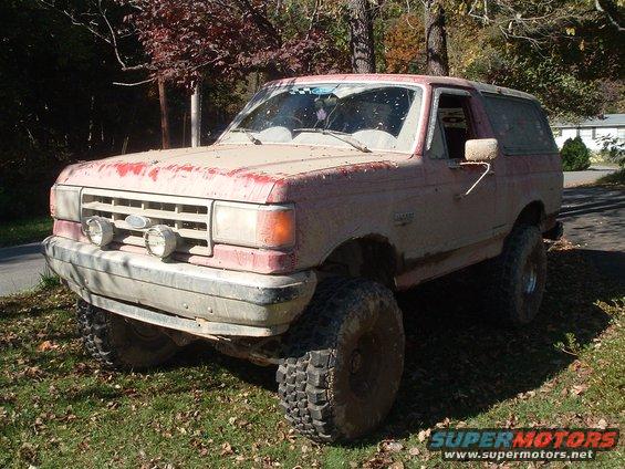 Mud-covered 1987 Ford Bronco parked on grassy area with trees in background