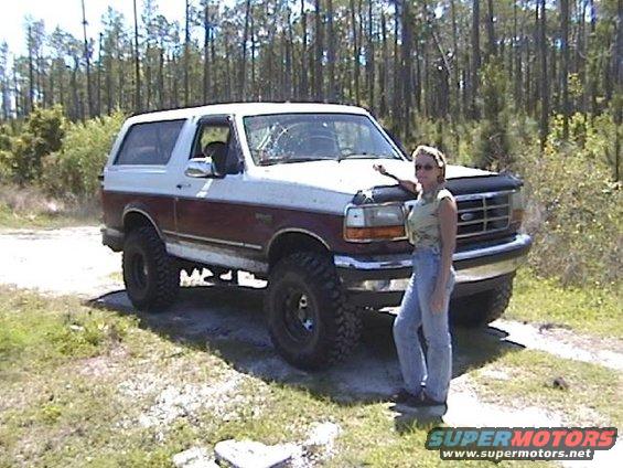 Two-tone white and maroon Ford Bronco with a woman standing next to it