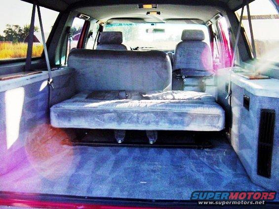 Van interior with seats and a mattress laid out in the back. Sunlight streams in