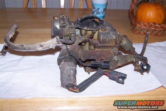 Used carburetor with hoses and electrical connectors, resting on a white cloth