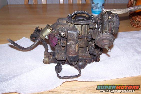 Holley carburetor with fuel line and electrical connectors attached, resting on white paper