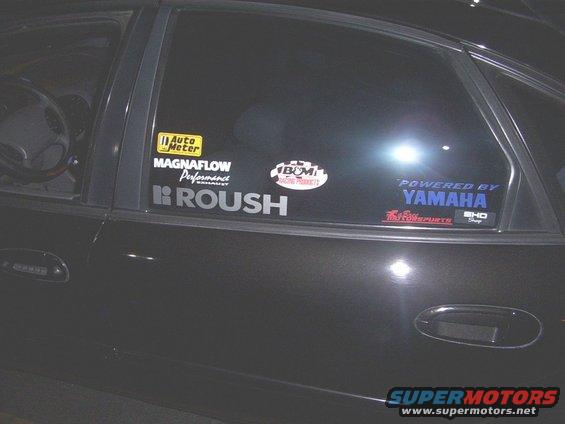Side view of a dark car with stickers like Auto Meter, Magnaflow, Roush, BOM, and Powered by Yamaha