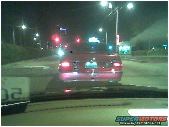 Red sedan driving at night, seen from behind. License plate is visible