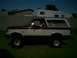 1988 Ford Bronco - A two-tone maroon and white Ford Bronco is parked on a grassy area in front of a brick wall and a trailer.