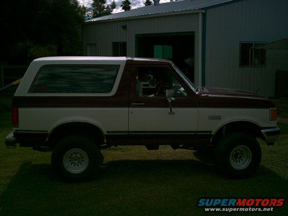 1988 Ford Bronco, two-tone maroon and white, parked in front of a metal building