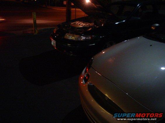 Black car with hood open, silver car front, at night