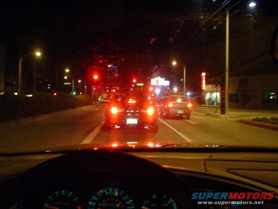 Dark sedan driving at night, rear view showing taillights and license plate area