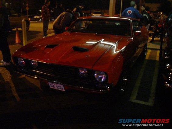 Red classic car with hood scoops and a license plate that says "OZ ROD"
