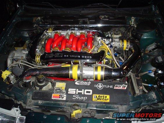 Green engine bay with red intake manifold, chrome accents, and yellow/black striped hoses. "SHO 24 VALVE DOHC" is visible