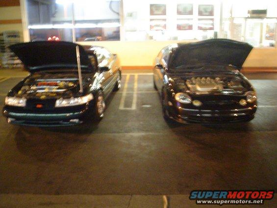 Two dark sedans parked side-by-side, hoods open, showing engines