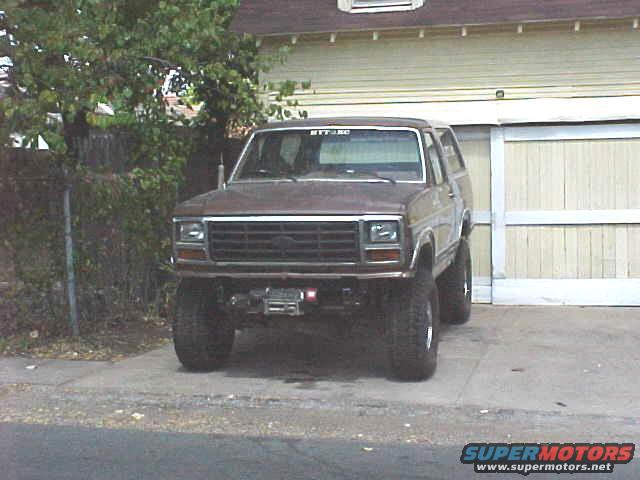 Brown Ford Bronco parked in front of a garage. It has a winch on the front bumper and aftermarket wheels