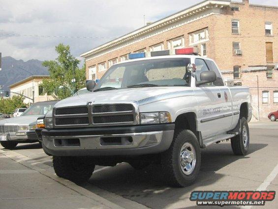 1994 Dodge Ram 1500 pickup truck, silver, with red and blue police lights on the roof. Text on door reads 'PROVO POLICE'. Another car is parked to the left