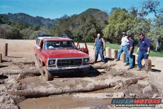 red SUV stuck in mud pit, guys watching