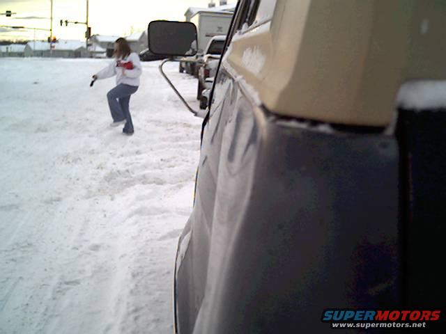 Person standing in snow next to the side of a dark-colored vehicle with a tan top