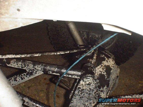 Close-up of greasy suspension parts and a blue wire under a vehicle