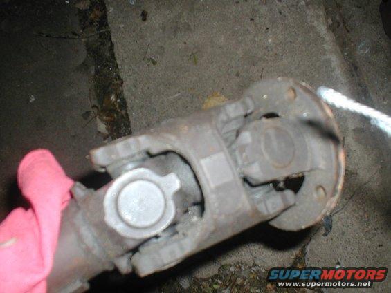 Driveshaft U-joint with a pink cloth nearby. Supermotors.net logo visible