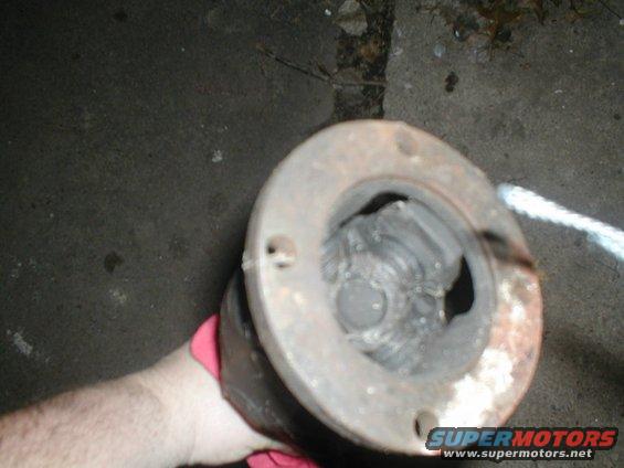 Close-up of a driveshaft U-joint with a hand wearing a pink glove holding it