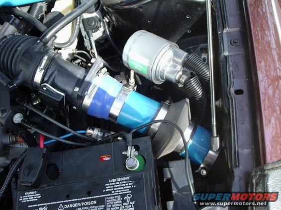 Close-up of engine bay showing blue intake piping, air filter housing, and battery