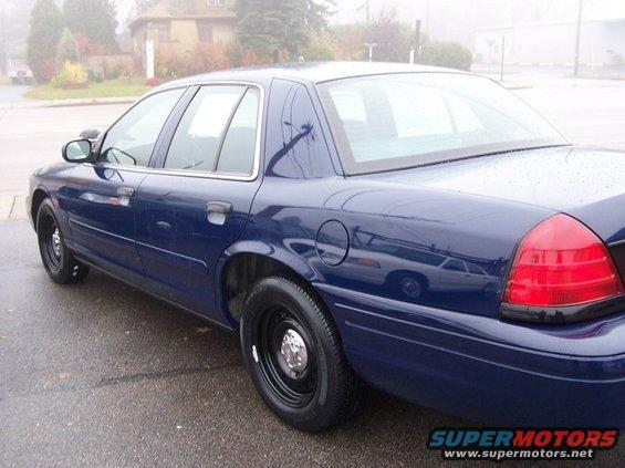 Dark blue sedan, likely a 2001 Ford Crown Victoria, parked on a wet street