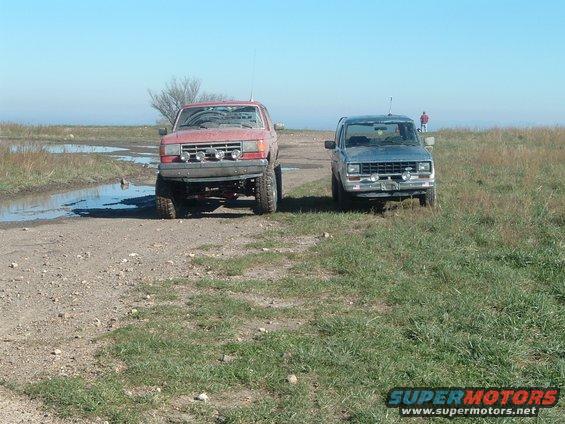red truck and blue truck parked on dirt road with puddles