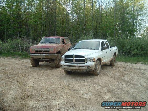 Red SUV and white pickup truck parked on dirt road with trees in background