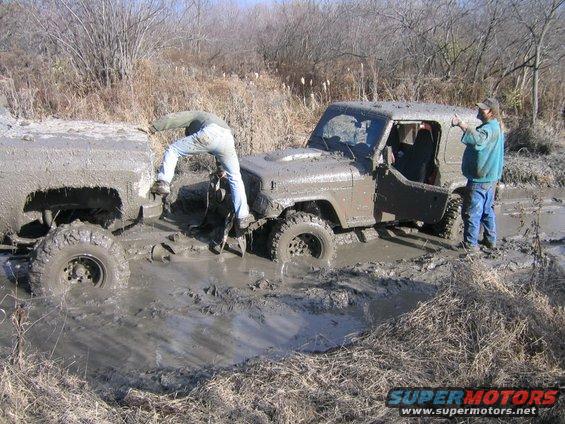 Muddy off-road vehicles stuck in swamp; people attempting rescue