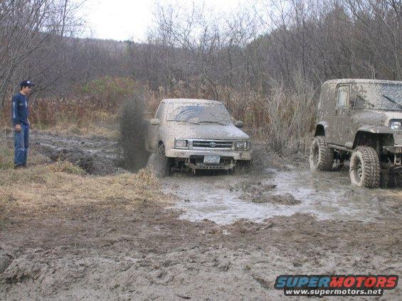 Mud-covered truck stuck in a muddy field with a person watching
