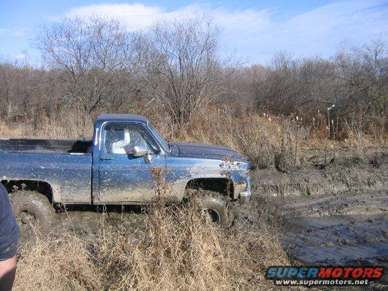 Blue pickup truck stuck in mud, front fender missing, side view