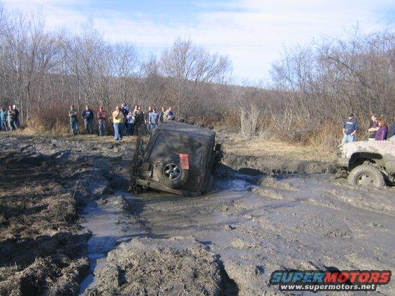 Two off-road vehicles are stuck deep in mud with spectators watching