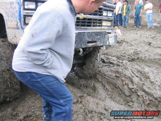guy looking at truck stuck in mud, other people watching