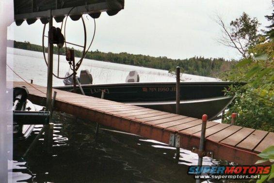 Dark green Lund boat with MN 1950 JI registration on a lake next to a wooden dock