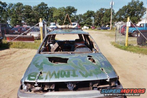 Damaged car with holes in hood, green paint, and chains attached
