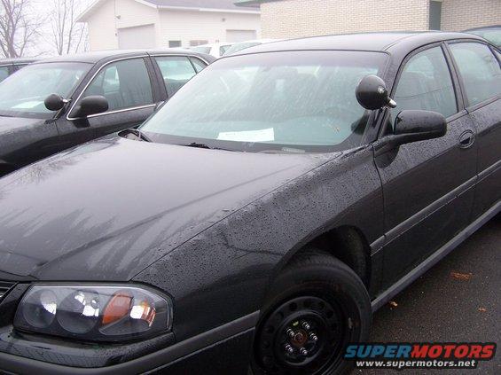 Black sedan, possibly a police car, parked next to another car. Has a spotlight on the driver's side