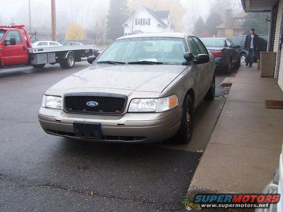Tan 2001 Ford Crown Victoria parked on wet asphalt, front view. Black grille with Ford logo